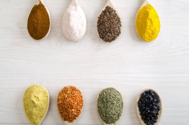 Beyaz ahşap zemin üzerinde tahta kaşıklar içinde farklı baharatlar