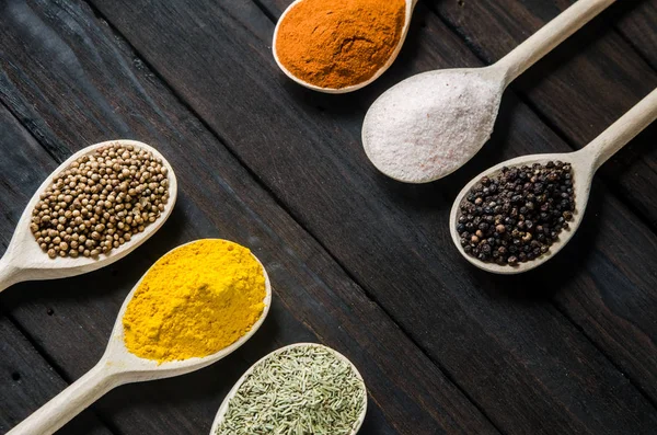 Different spices in wooden spoons on a black wooden background — Stock Photo, Image