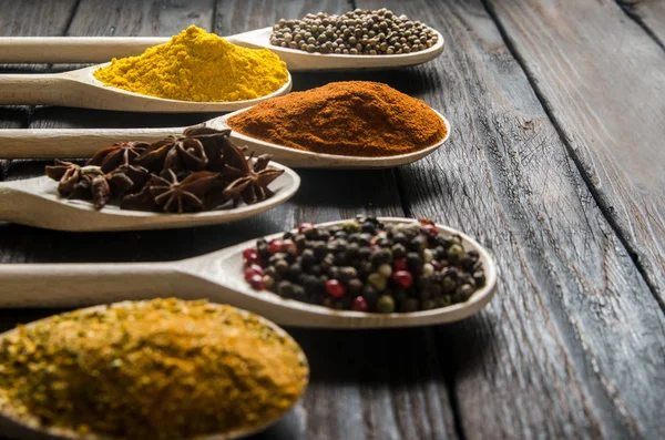 Different spices in wooden spoons on a black wooden background — Stock Photo, Image