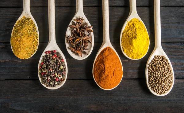 Different spices in wooden spoons on a black wooden background — Stock Photo, Image