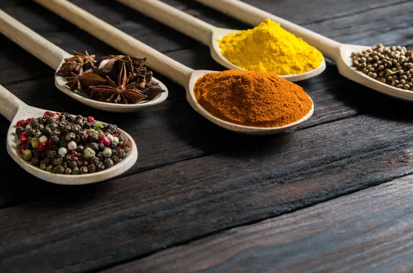 Different spices in wooden spoons on a black wooden background — Stock Photo, Image