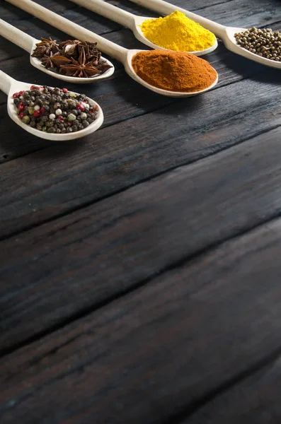 Diferentes especias en cucharas de madera sobre un fondo de madera negro — Foto de Stock