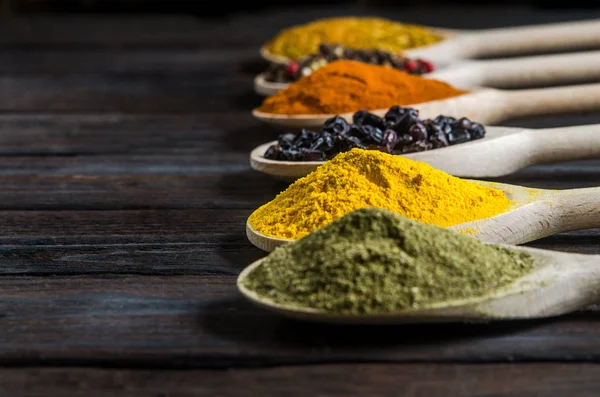 Different spices in wooden spoons on a black wooden background — Stock Photo, Image