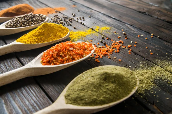 Different spices in wooden spoons on a black wooden background — Stock Photo, Image