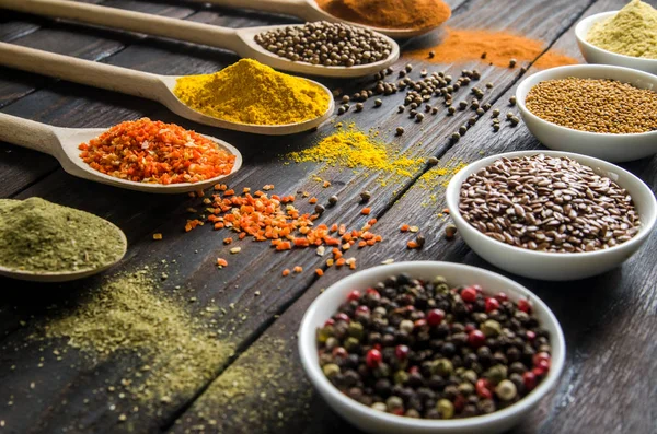 Different spices in wooden spoons on a black wooden background — Stock Photo, Image