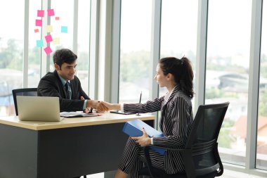Ofisteki toplantıda siyah takım elbiseli genç işverenler el sıkışıyor. İş görüşmesinden sonra ortam çok güzel..