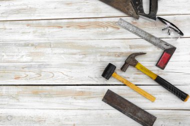 Ahşap işçiliği ekipmanları ahşap zeminde düzgünce düzenlenmiştir. Sipariş edildiği gibi, el testeresi, toz geçirmez gözlükler, makinist kare, çekiç, çekiç, çekiç, dovetail testere.