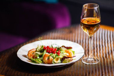 Bir bardak şarap bir içkiyle masaya bir tabak güzel iştah açıcı salata taze sebze, karides, bıldırcın yumurtası ve lingonberries olduğunu.