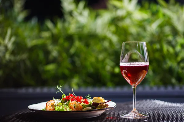 Bir bardak şarap bir içkiyle masaya bir tabak güzel iştah açıcı salata taze sebze, karides, bıldırcın yumurtası ve lingonberries olduğunu.