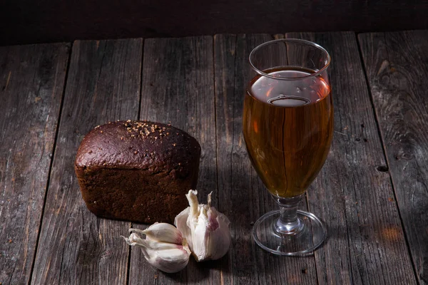 Szklanka piwa lekkie, bochenek chleb czarny i czosnek leżą na t — Zdjęcie stockowe