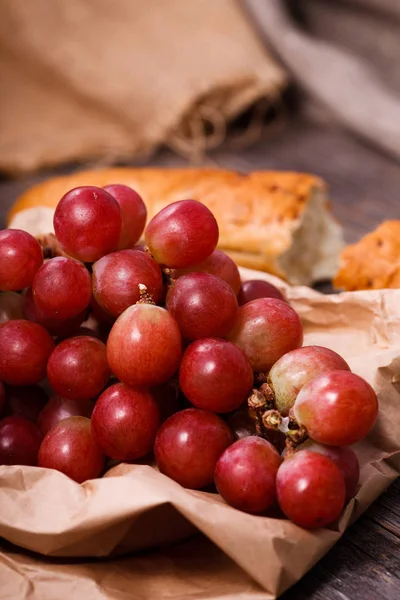 A bunch of juicy large red grapes and fresh crispy wheaten bague — Stock Photo, Image