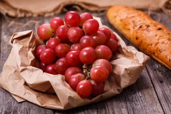 A bunch of juicy large red grapes and fresh crispy wheaten bague — Stock Photo, Image