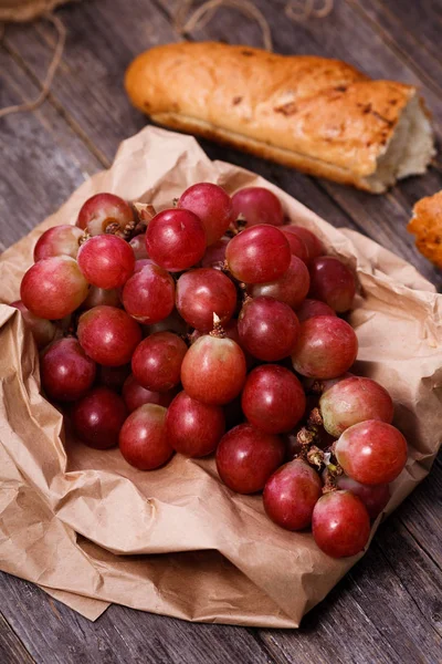 A bunch of juicy large red grapes and fresh crispy wheaten bague — Stock Photo, Image