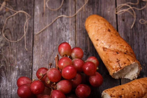 A bunch of juicy large red grapes and fresh crispy wheaten bague — Stock Photo, Image