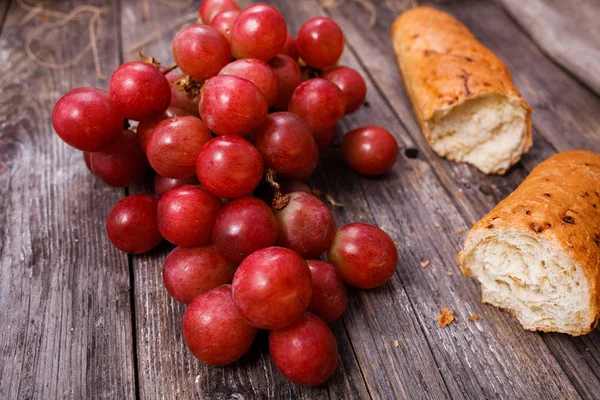 A bunch of juicy large red grapes and fresh crispy wheaten bague — Stock Photo, Image