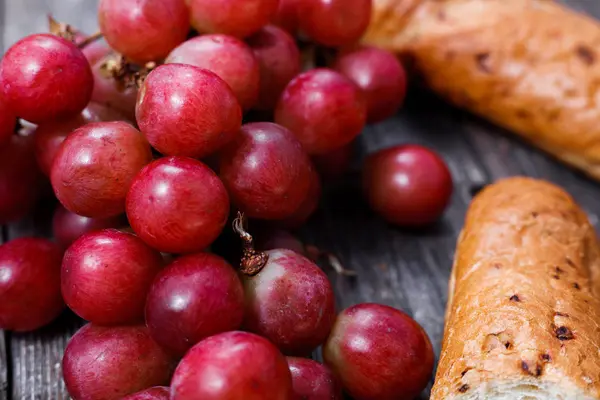 A bunch of juicy large red grapes and fresh crispy wheaten bague — Stock Photo, Image