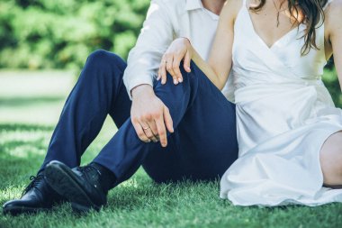 Gelin ve damat beyaz düğün elbise ve mavi pantolon birlikte çimlerde oturuyor