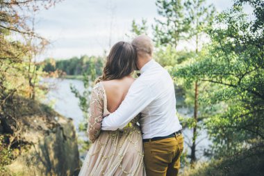 Çift birbirlerine sarılma ve bej güzel elbise beyaz gömlek ve sarı pantolon kel doğada üzerinde seyir
