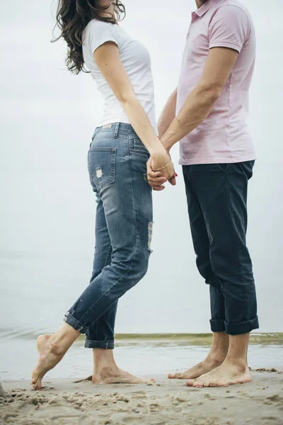 couple in jeans and white and pink shirt are staying on the seaside holding their hands