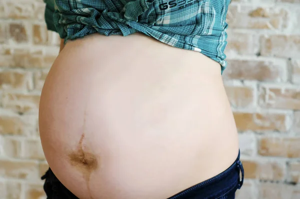 Беременный живот в джинсах и рубашке — стоковое фото