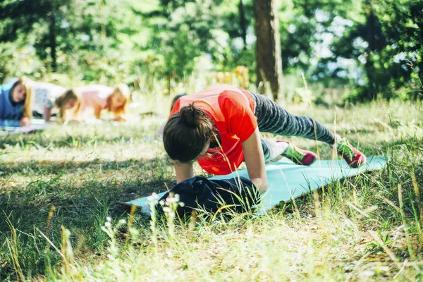 woman in orange shirt training fitness on the fitness mat in the forest