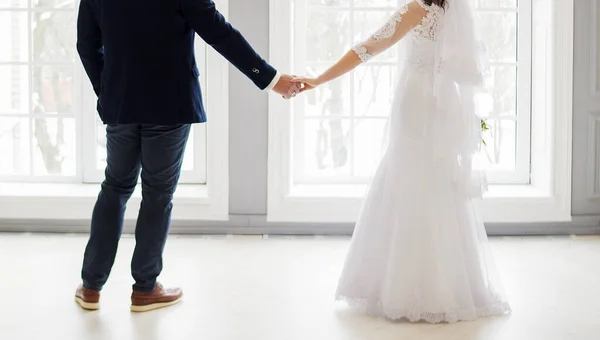 新娘和新郎 身穿白色婚纱和蓝色服装 手牵手靠近窗户 在室外过冬 — 图库照片