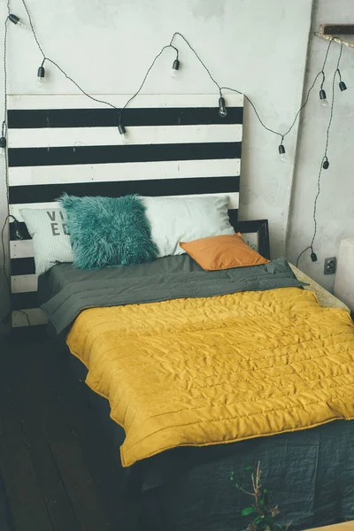 グレーの色合いでミニマリズム快適なベッド 大きな黄色のシエナラグとターコイズと白い枕と 部屋には電球が飾られています — ストック写真