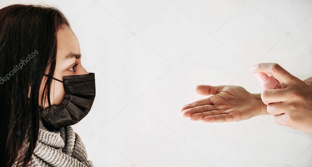 Woman in black medical masks and cleaning hands with sanitizer. Light background. Coronavirus covid19 epidemic pandemic concept.