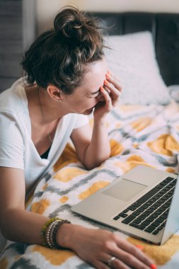 Kız dizüstü bilgisayarın yanında oturuyor ve gülüyor, elleriyle yüzünü örtüyor. Karantinadaki akrabalarla çevrimiçi iletişim kurmak mutluluk ve olumlu duygular getirir. Arkadaşlarla komik sohbetler