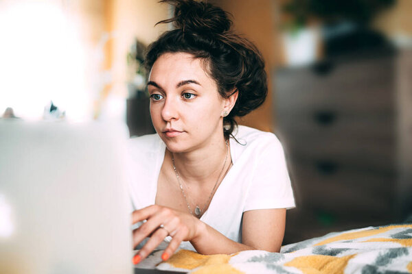 Счастливая молодая женщина сидит дома с ноутбуком на кровати. Хорошие новости карантина. Забота о родственниках. Успешная сделка на работе. Радостное общение. Закрыть
