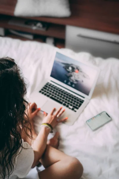 A young woman is sitting on the bed with a laptop and a phone. View from above. Work from home. Stay home concept. Remote work. Work online. Business online. Hanging out at home with a computer.