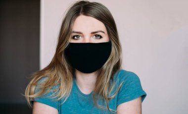 Açık arkaplanda siyah tıbbi maske takan turkuaz tişörtlü genç bir kadının yakın plan portresi. Virüs koruması. Coronovirus covid-19 konsepti karantina. Evde kal.