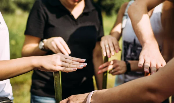 People stand in a circle and hold hands on a wooden stick.