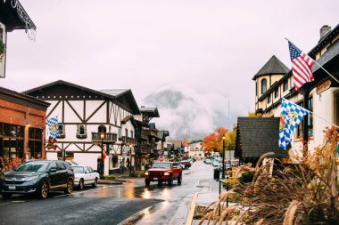 Leavenworth USA Washington - 25 Ekim 2017: Binalar, dükkanlar, arabalar, bayraklar ve insanlarla şehir manzarası. Yağmurlu sisli bir gün