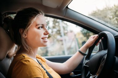  Arabanın direksiyonunda oturan genç ve güzel bir kız emniyet kemeri takmış ve yola bakıyor, gülümsüyor. Yakın plan. Sarı tişört ve sarı saç. Arabayla seyahat et. Araba sürmekten zevk alıyorum.