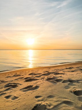  Deniz kenarında şafak vakti. Küçük dalgalarla sakin bir su. Güneşin suyun üzerindeki yansıması. Kumda bulutlar ve ayak izleri olan temiz bir gökyüzü. Mükemmel sabah.