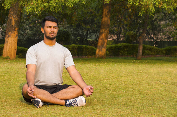 Young guy doing yoga lotus pose in a park