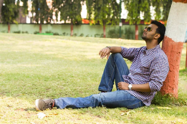 Young man wearing sunglasses relaxing and leaning against tree — Stock Photo, Image