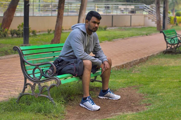 Jonge sporter zittend op een houten bankje in een park — Stockfoto