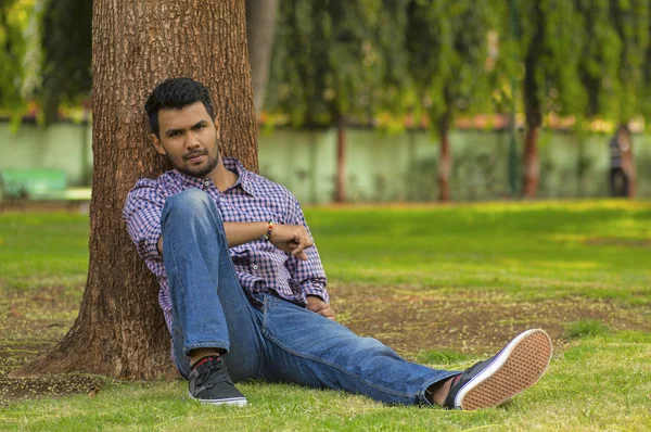 나무에 기대어 잔디에 앉아 젊은 세련 된 행복 한 사람 — 스톡 사진