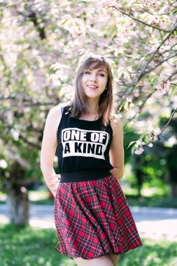 Sakura çiçeklenme tree yakınındaki genç güzel kadın. Pembe çiçekler, Bahar ve gençlik kavramı. Şık kız gülümsüyor. Kiraz ağacı ile Bahçe çiçek açmış. Copyplace, metin için yer.