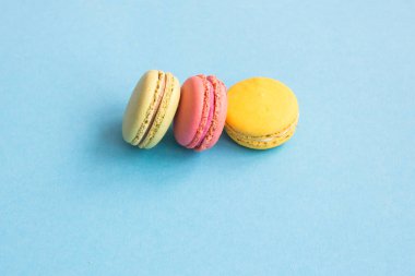 Macaroons, pembe, sarı ve yeşil bademli kurabiye mavi zemin üzerine. Parlak ve renkli kavramı. Copyplace, metin için yer. 