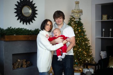 Anne, baba ve bebek Noel tatilinde evde sarılıyor.