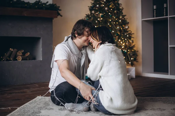 Ung söt söt par i kärlek kyssas i julafton nära träd med presenter hemma i december. — Stockfoto