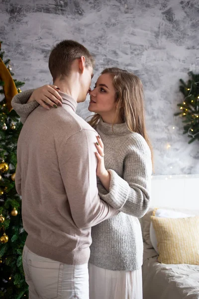 Pareja enamorada cerca de la cama de pie junto a un árbol de Navidad en casa — Foto de Stock