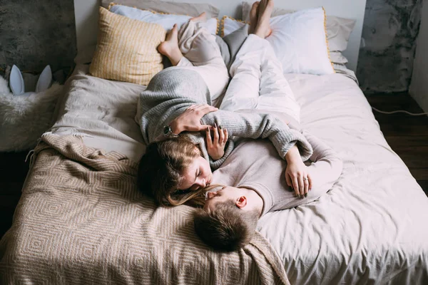 Jovem casal bonito marido e sua bela esposa abraçando na cama no quarto — Fotografia de Stock