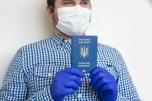 Man in mask on white background with Ukrainian passport in his hands. Coronavirus, illness, infection, quarantine, medical mask