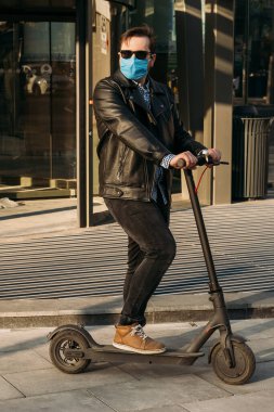 Sokakta elektrikli scooter 'da koruyucu maske takan bir adam. Grip olmuş, maske takan hasta bir adam. Sokakta salgın hastalık konsepti..
