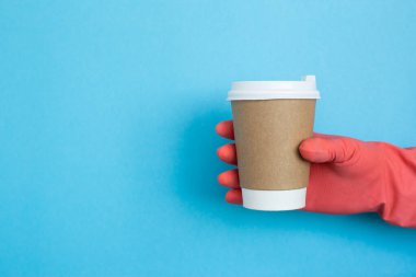 Mavi arka planda pembe tıbbi eldivenli kahve fincanı. Kağıt bardakta kadın eli. Kahve fincanı tutan bir kadın eli. Uzayı kopyala Coronavirus koruması