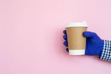 Elinde kahve fincanı pembe arka planda izole edilmiş. Kâğıt bardakla. Kahve fincanı tutan bir kadın eli. Boşluğu kopyala, koronavirüs koruması